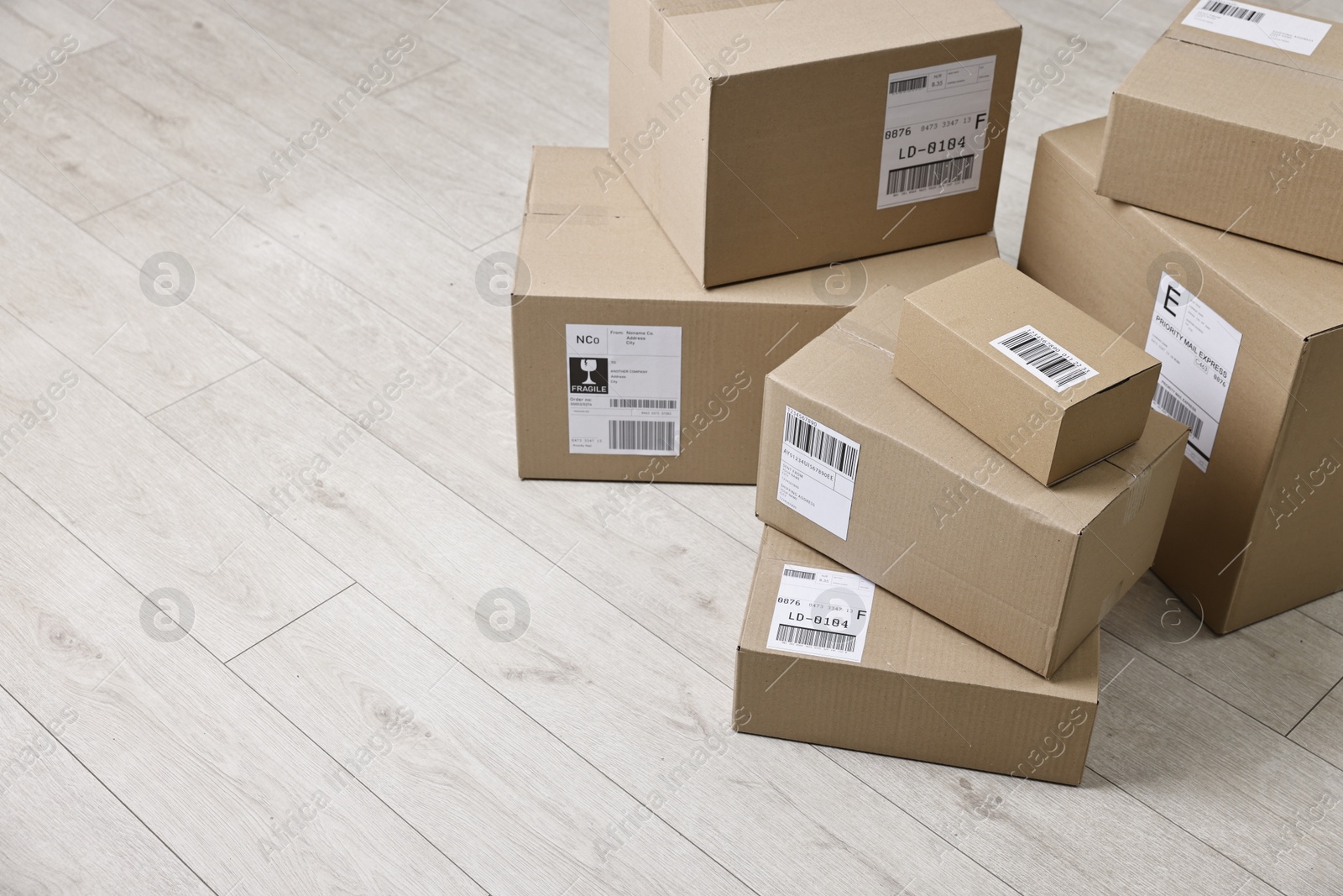 Photo of Cardboard parcel boxes with shipping labels on floor indoors, space for text