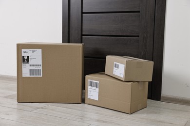 Photo of Cardboard parcel boxes with shipping labels near door indoors