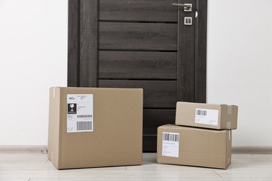 Photo of Cardboard parcel boxes with shipping labels near door indoors