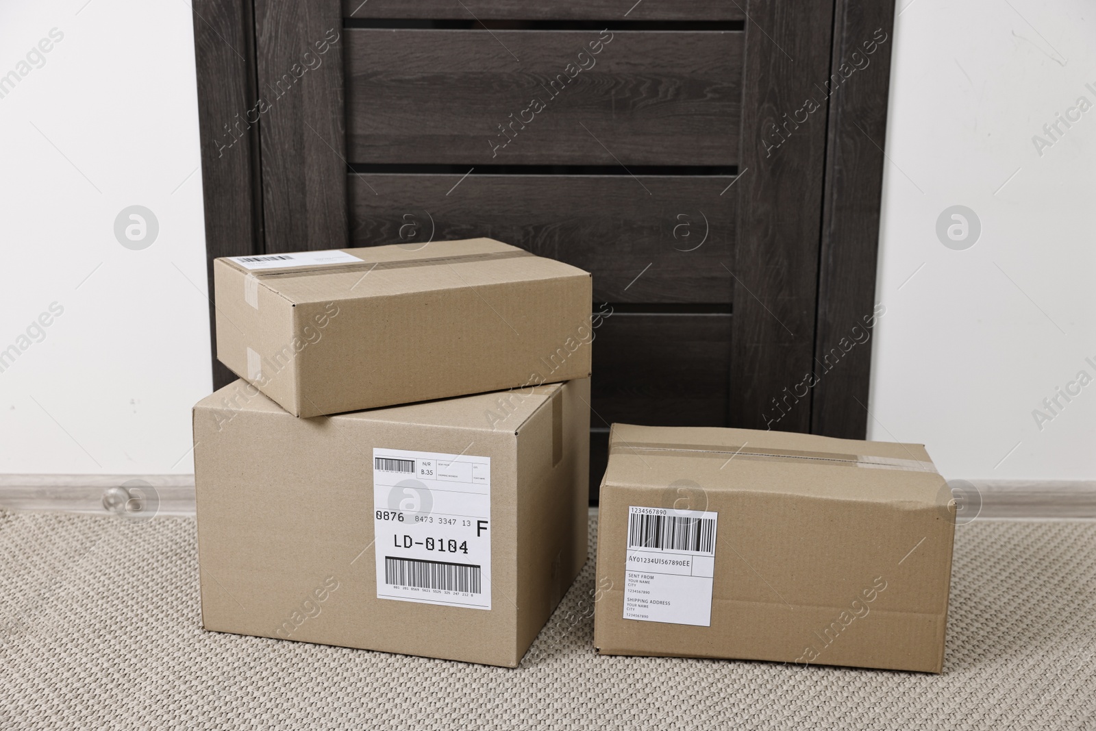 Photo of Cardboard parcel boxes with shipping labels near door indoors