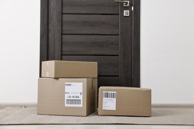 Photo of Cardboard parcel boxes with shipping labels near door indoors