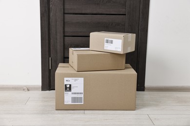 Photo of Cardboard parcel boxes with shipping labels near door indoors