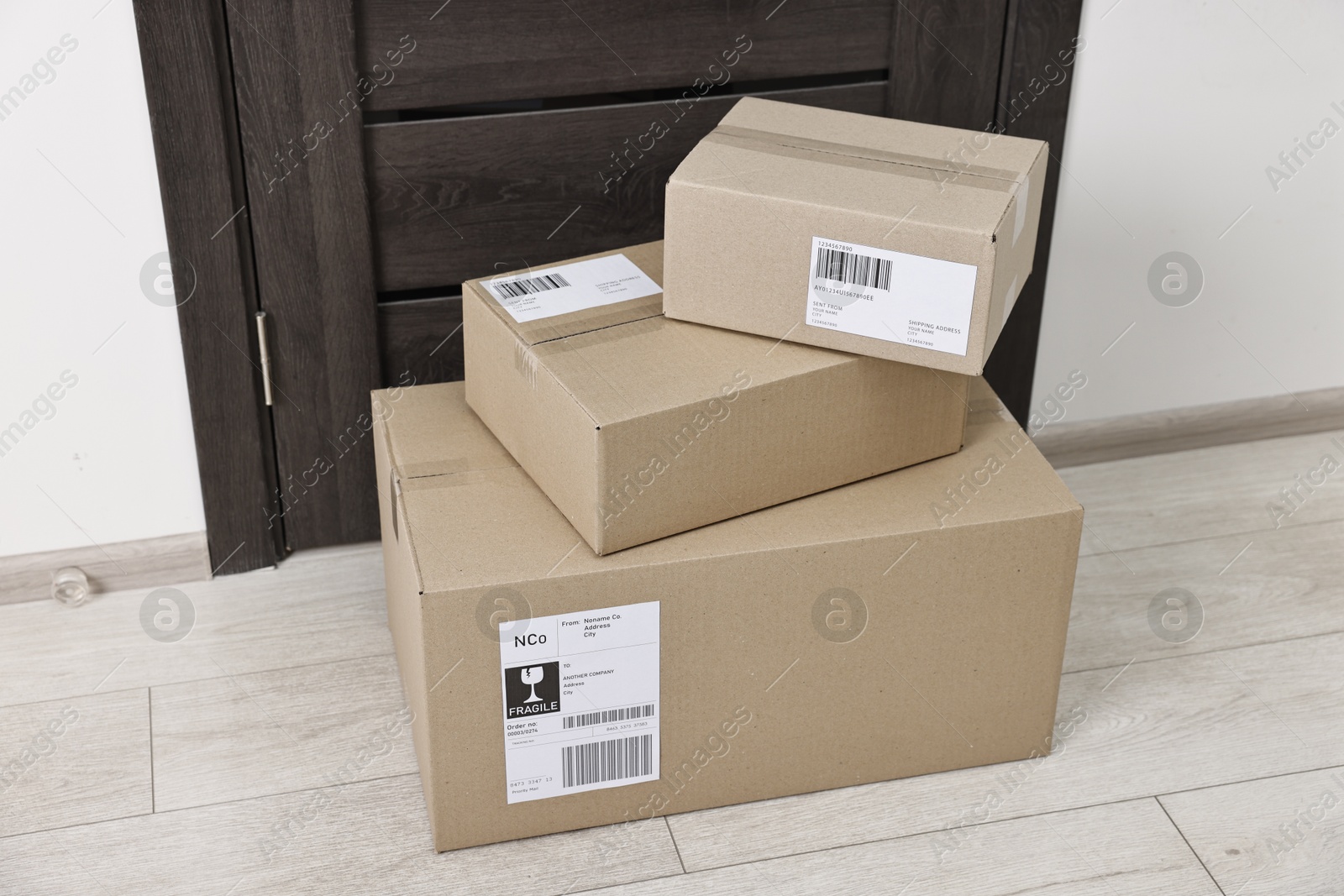 Photo of Cardboard parcel boxes with shipping labels near door indoors