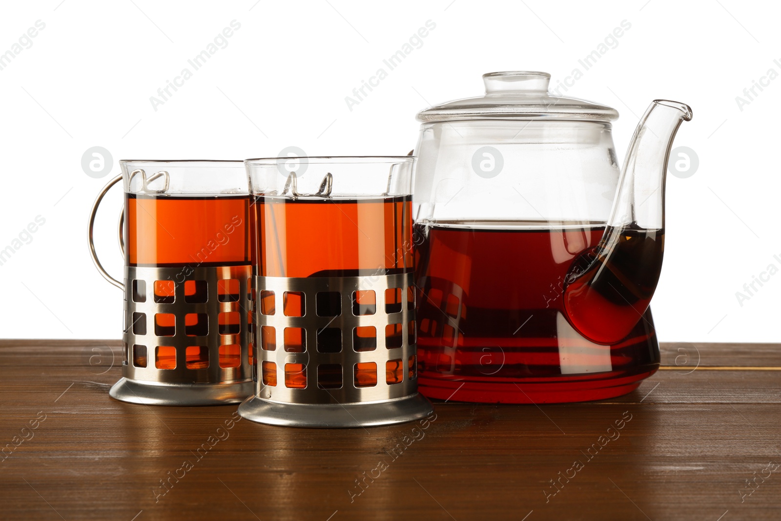 Photo of Glasses of aromatic tea in holders and teapot on wooden table against white background