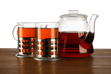 Glasses of aromatic tea in holders and teapot on wooden table against white background