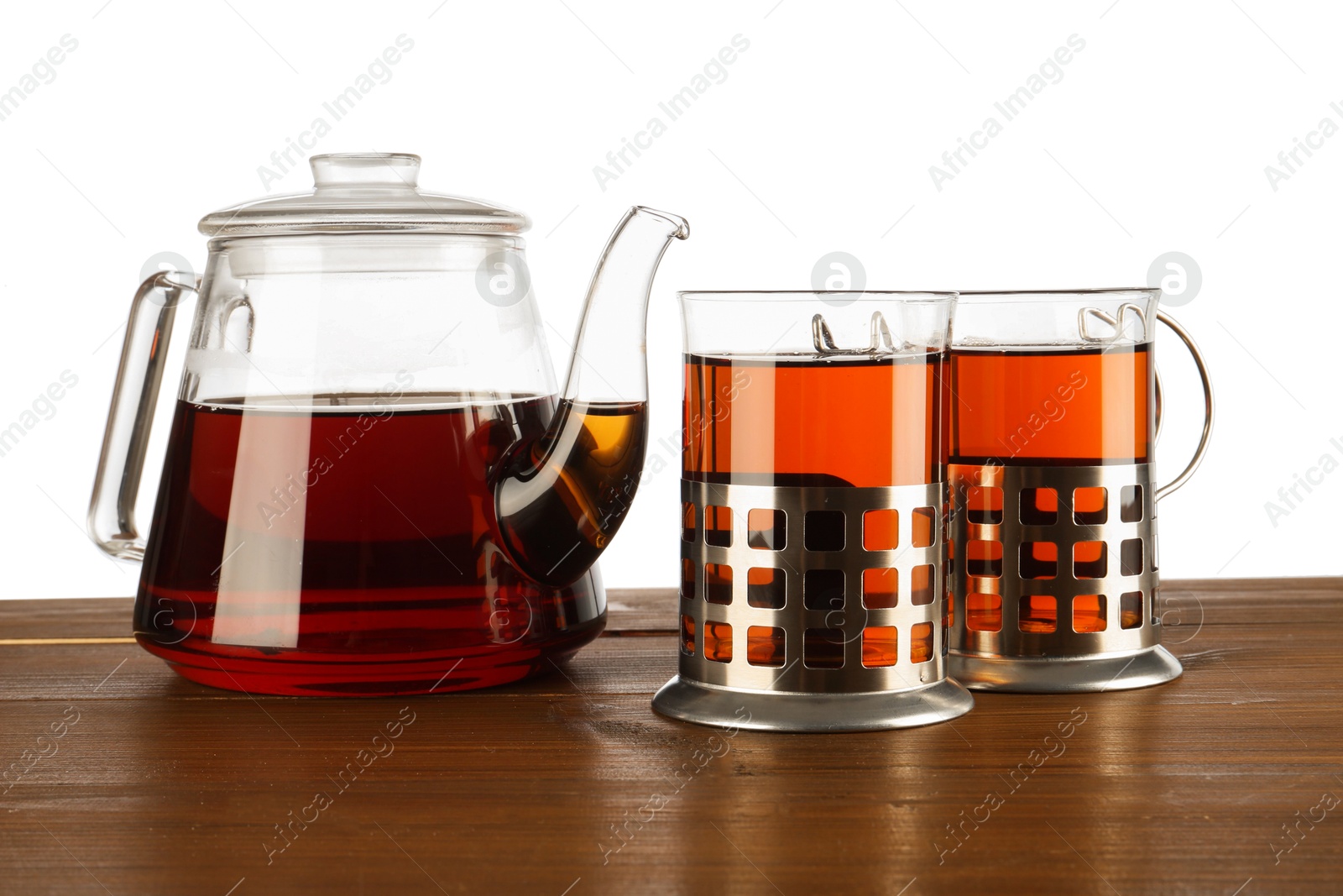 Photo of Glasses of aromatic tea in holders and teapot on wooden table against white background