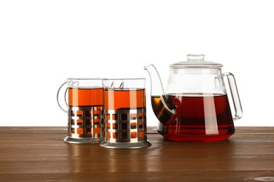 Glasses of aromatic tea in holders and teapot on wooden table against white background