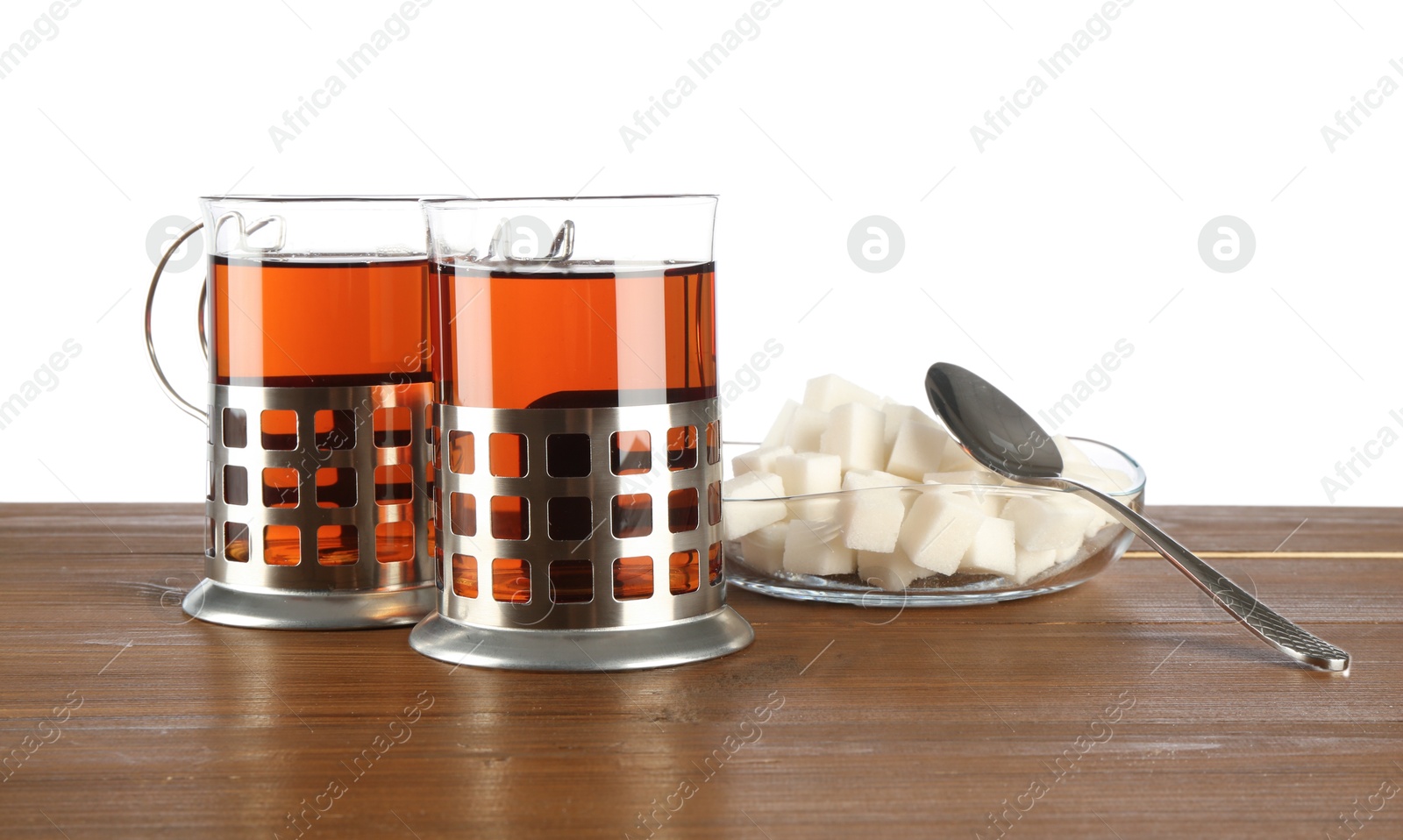 Photo of Glasses of aromatic tea in holders, sugar cubes and spoon on wooden table against white background