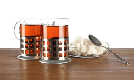 Photo of Glasses of aromatic tea in holders, sugar cubes and spoon on wooden table against white background