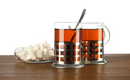 Photo of Glasses of aromatic tea in holders, sugar cubes and spoon on wooden table against white background