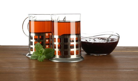 Photo of Glasses of aromatic tea in holders, mint and jam on wooden table against white