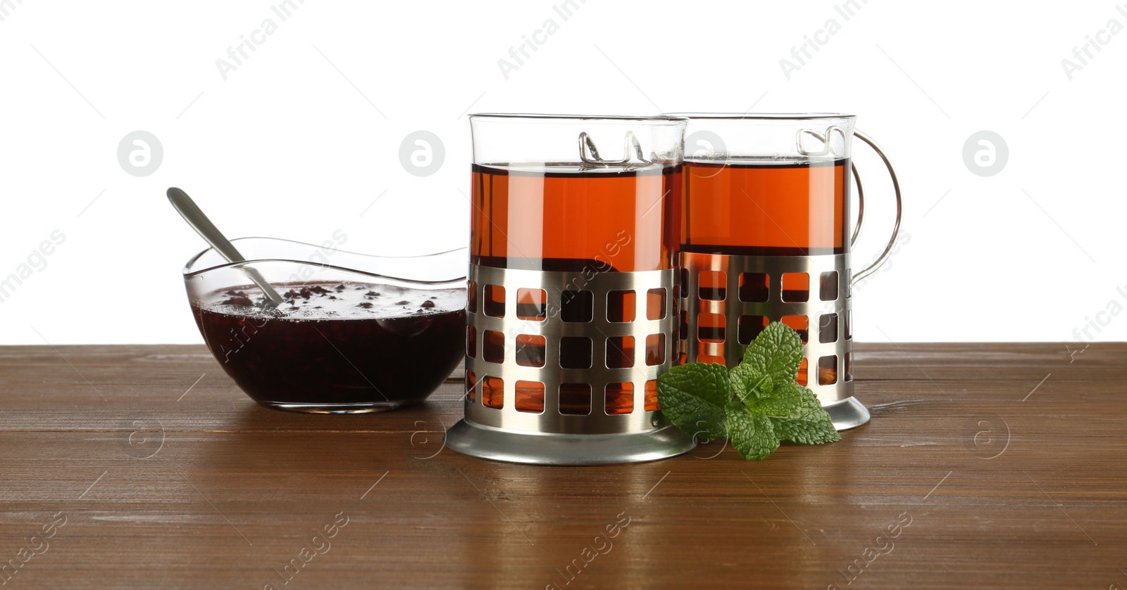 Photo of Glasses of aromatic tea in holders, mint and jam on wooden table against white