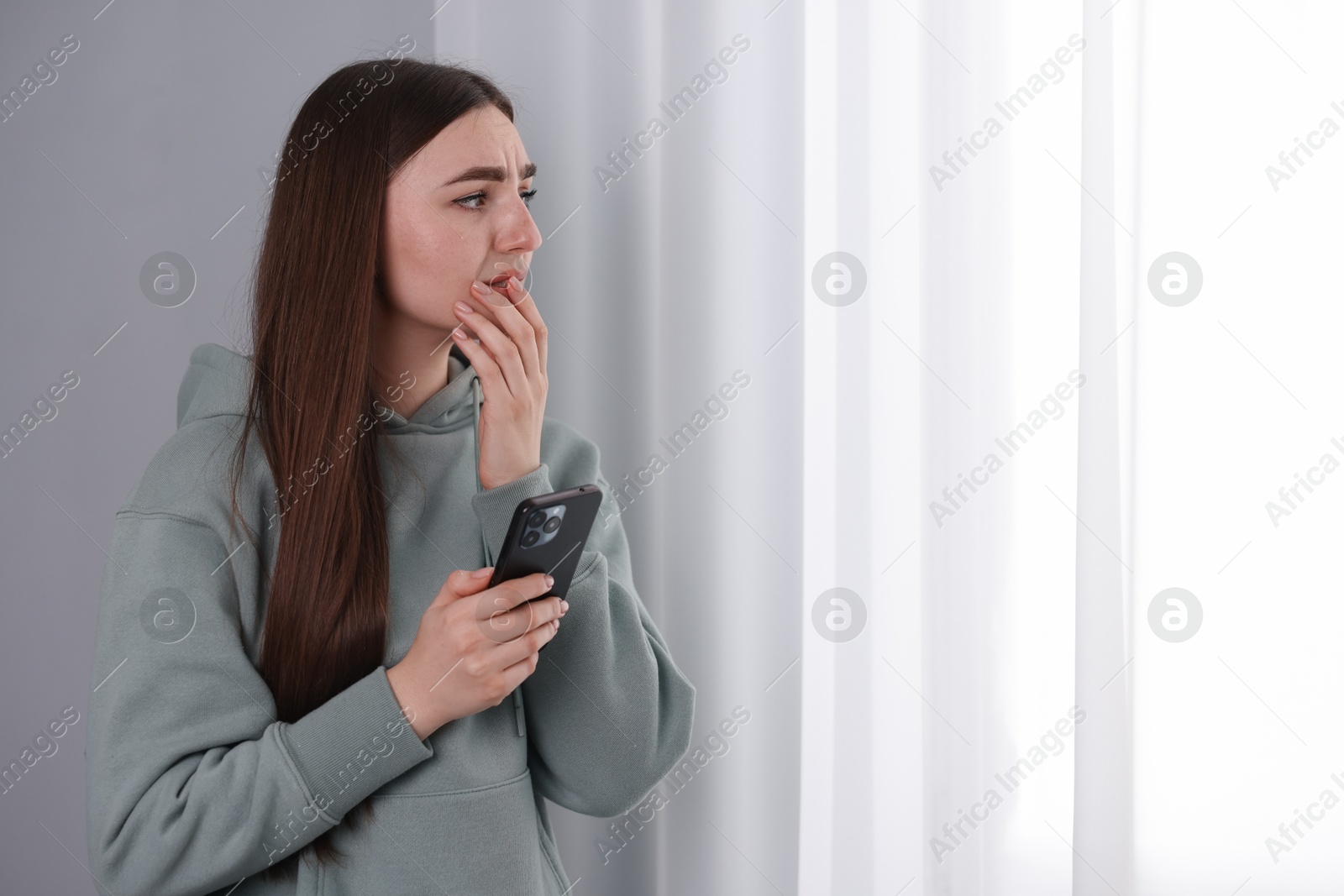 Photo of Desperate woman calling hotline for mental health help near window at home. Space for text