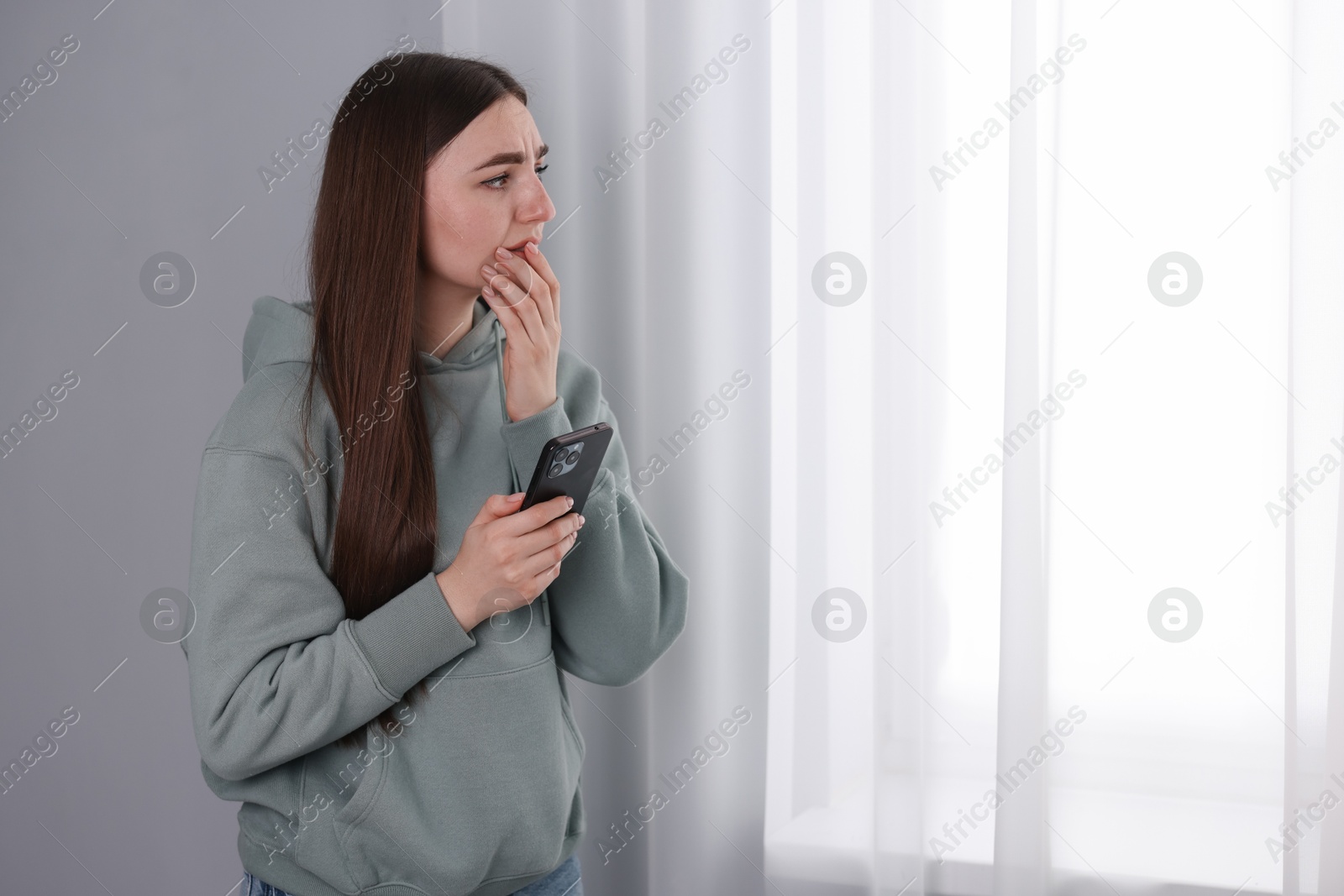 Photo of Desperate woman calling hotline for mental health help near window at home. Space for text