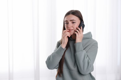 Photo of Desperate woman calling hotline for mental health help near window at home. Space for text