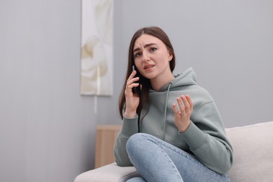 Photo of Depressed woman calling hotline for mental health help on sofa at home