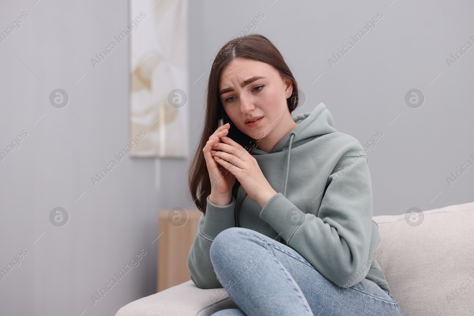 Photo of Depressed woman calling hotline for mental health help on sofa at home