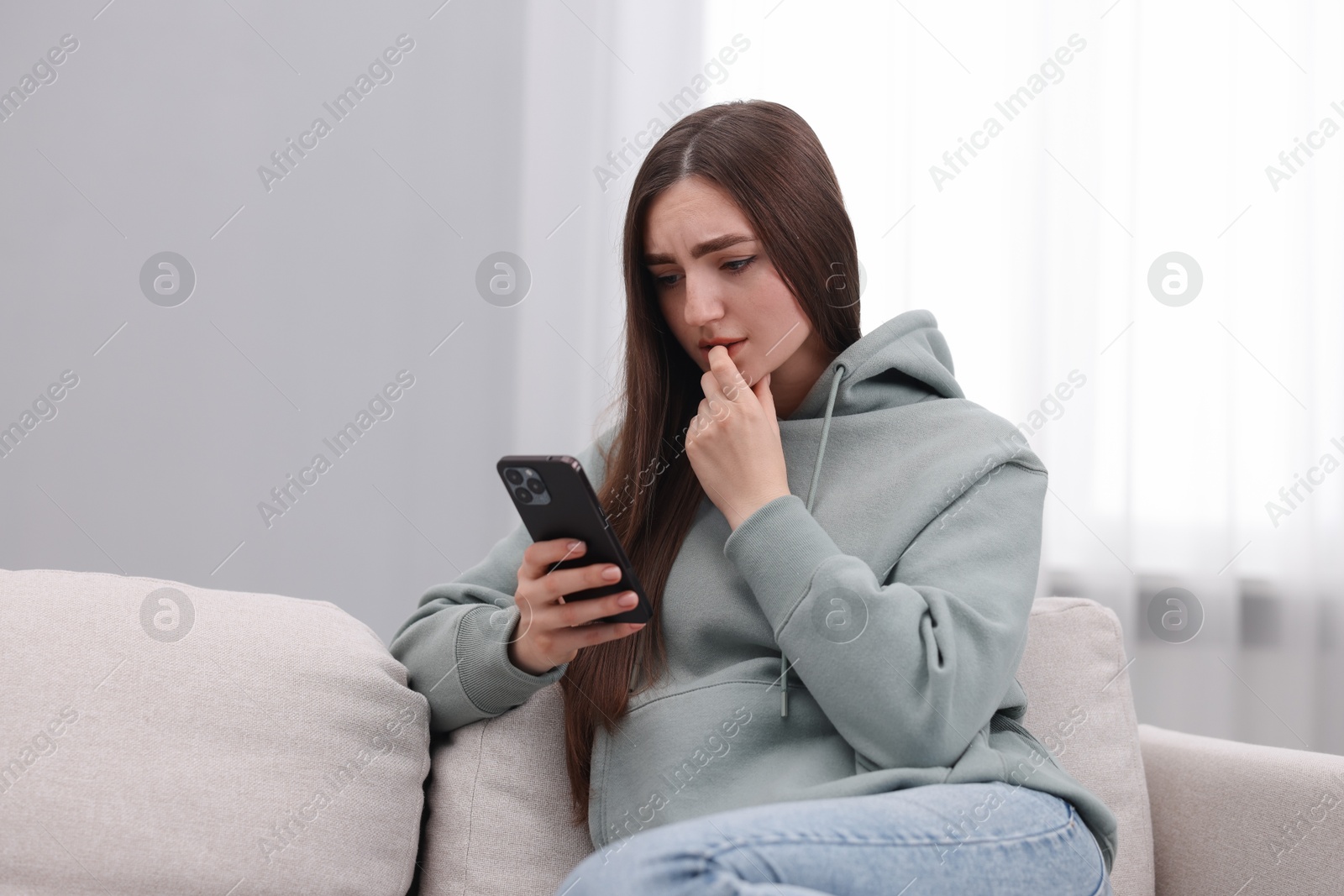 Photo of Depressed woman calling hotline for mental health help on sofa at home