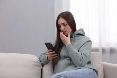 Photo of Depressed woman calling hotline for mental health help on sofa at home. Space for text