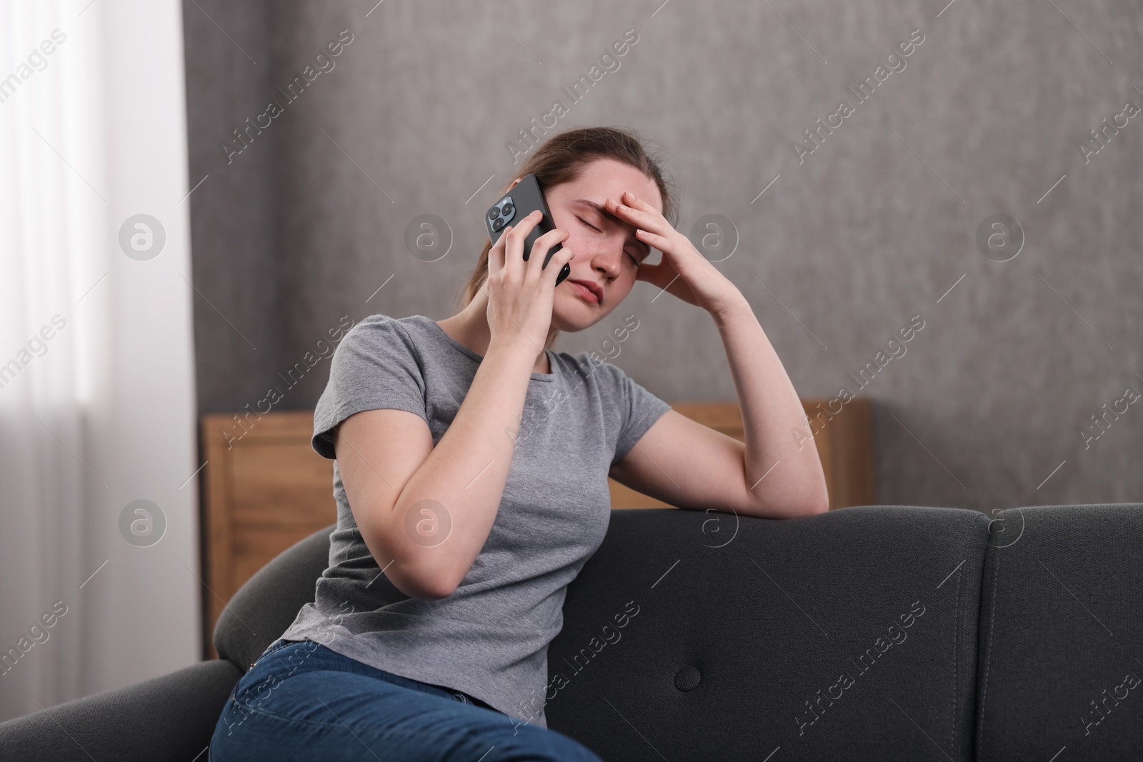 Photo of Depressed woman calling hotline for mental health help on sofa at home