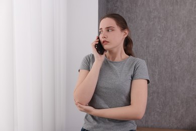 Photo of Stressed woman calling hotline for mental health help near window at home