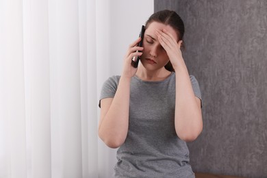 Photo of Stressed woman calling hotline for mental health help near window at home. Space for text