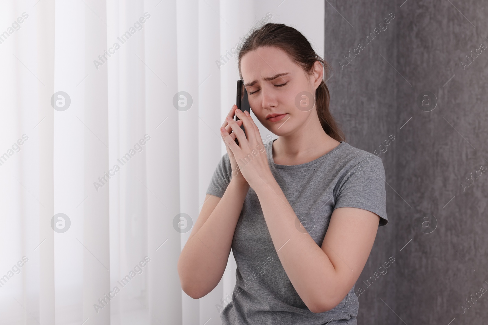 Photo of Stressed woman calling hotline for mental health help near window at home. Space for text