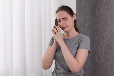 Photo of Stressed woman calling hotline for mental health help near window at home. Space for text