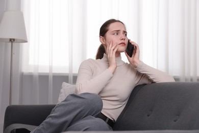 Photo of Depressed woman calling hotline for mental health help on sofa at home