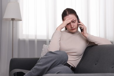 Photo of Depressed woman calling hotline for mental health help on sofa at home