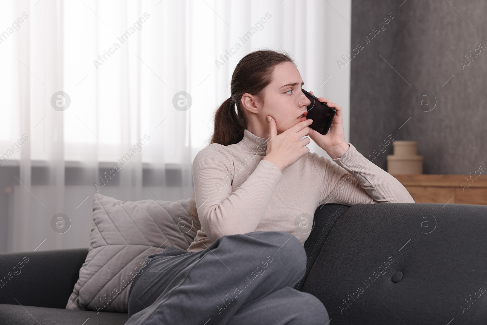 Photo of Depressed woman calling hotline for mental health help on sofa at home