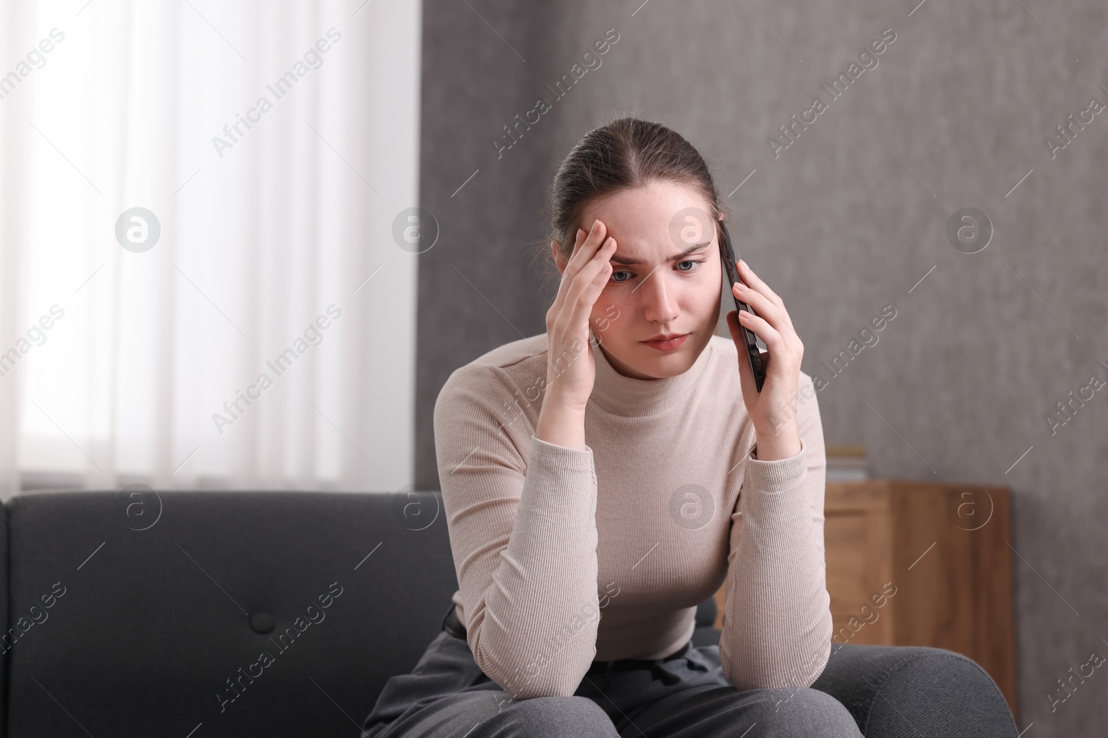 Photo of Depressed woman calling hotline for mental health help on sofa at home