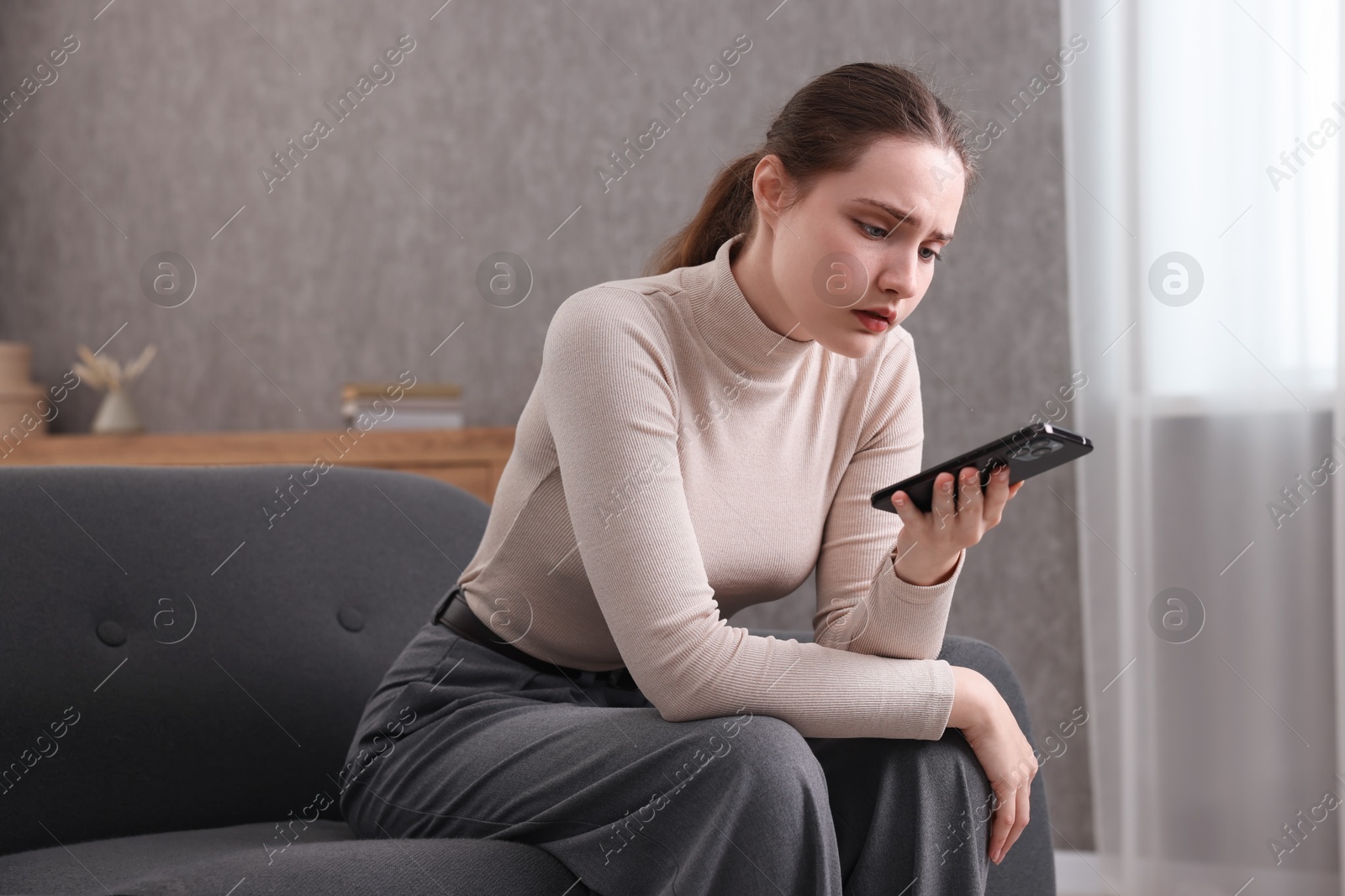 Photo of Depressed woman calling hotline for mental health help on sofa at home