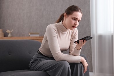 Photo of Depressed woman calling hotline for mental health help on sofa at home