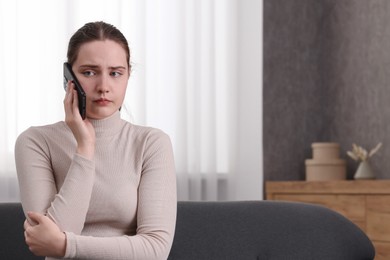 Photo of Depressed woman calling hotline for mental health help on sofa at home. Space for text