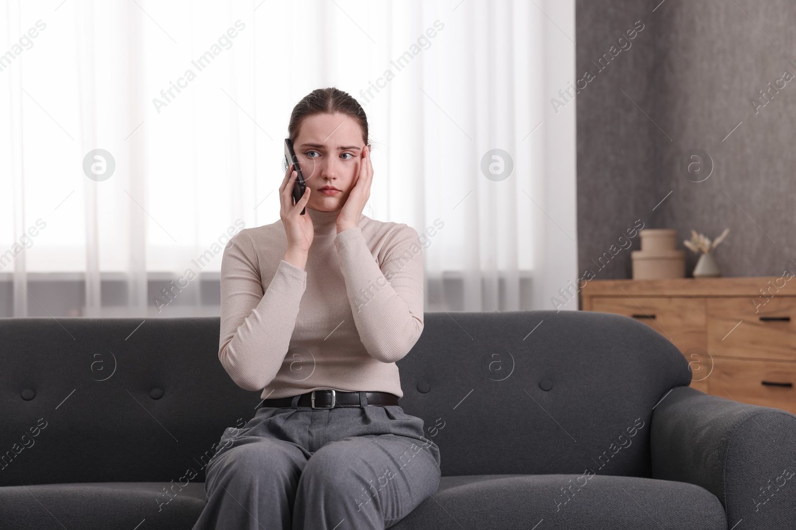 Photo of Depressed woman calling hotline for mental health help on sofa at home