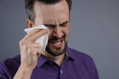 Sad man with paper tissue crying on grey background