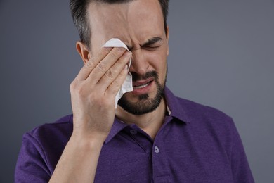 Sad man with paper tissue crying on grey background