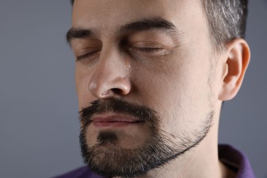 Sad man crying on grey background, closeup