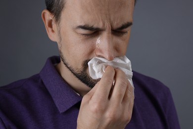 Sad man with paper tissue crying on grey background