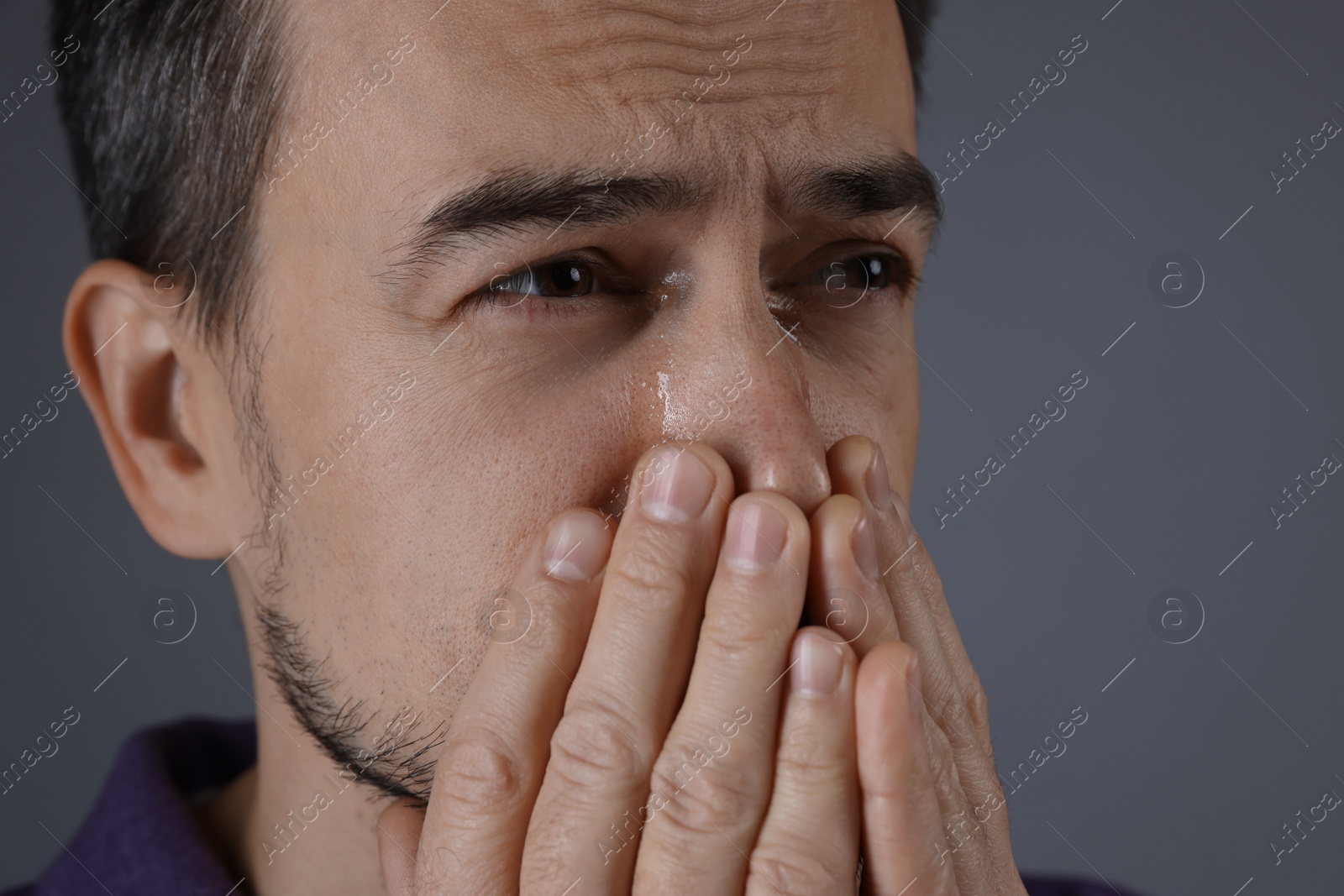 Photo of Sad man crying on grey background, closeup