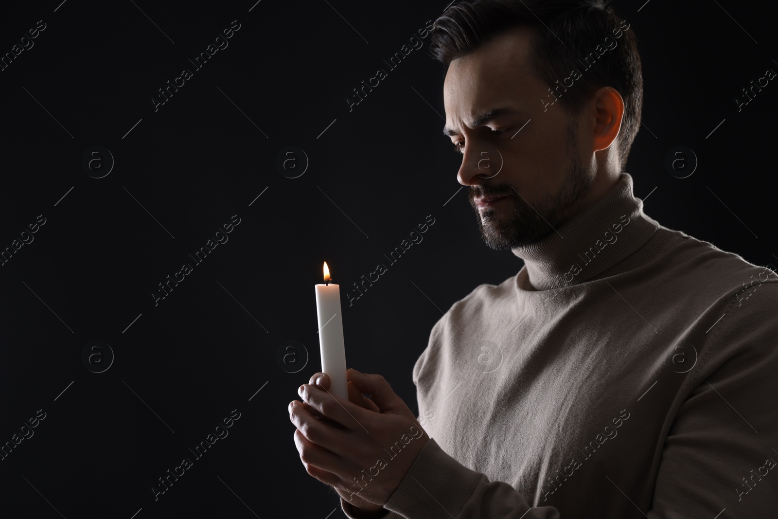 Photo of Sad man with burning candle crying on black background, space for text