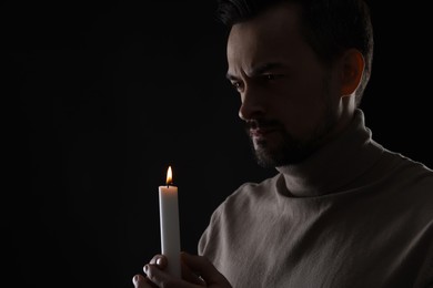 Photo of Sad man with burning candle crying on black background, space for text