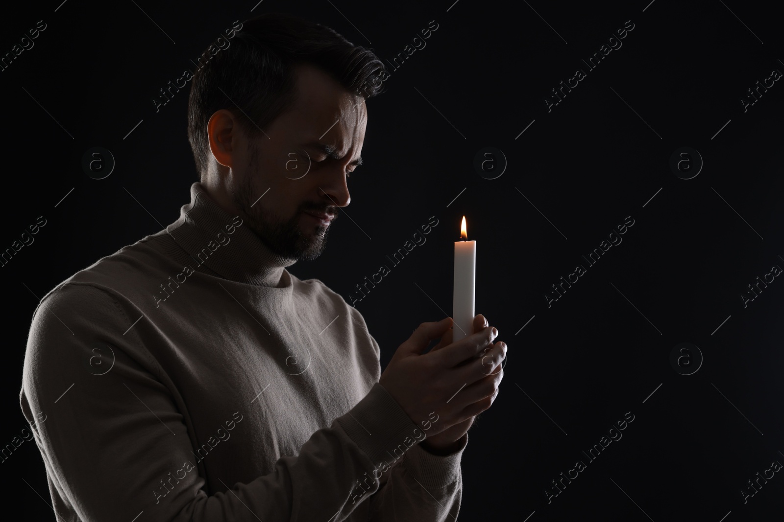 Photo of Sad man with burning candle crying on black background, space for text