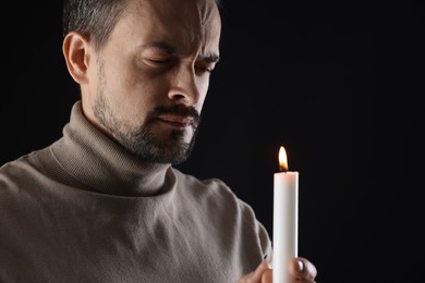 Photo of Sad man with burning candle crying on black background, space for text