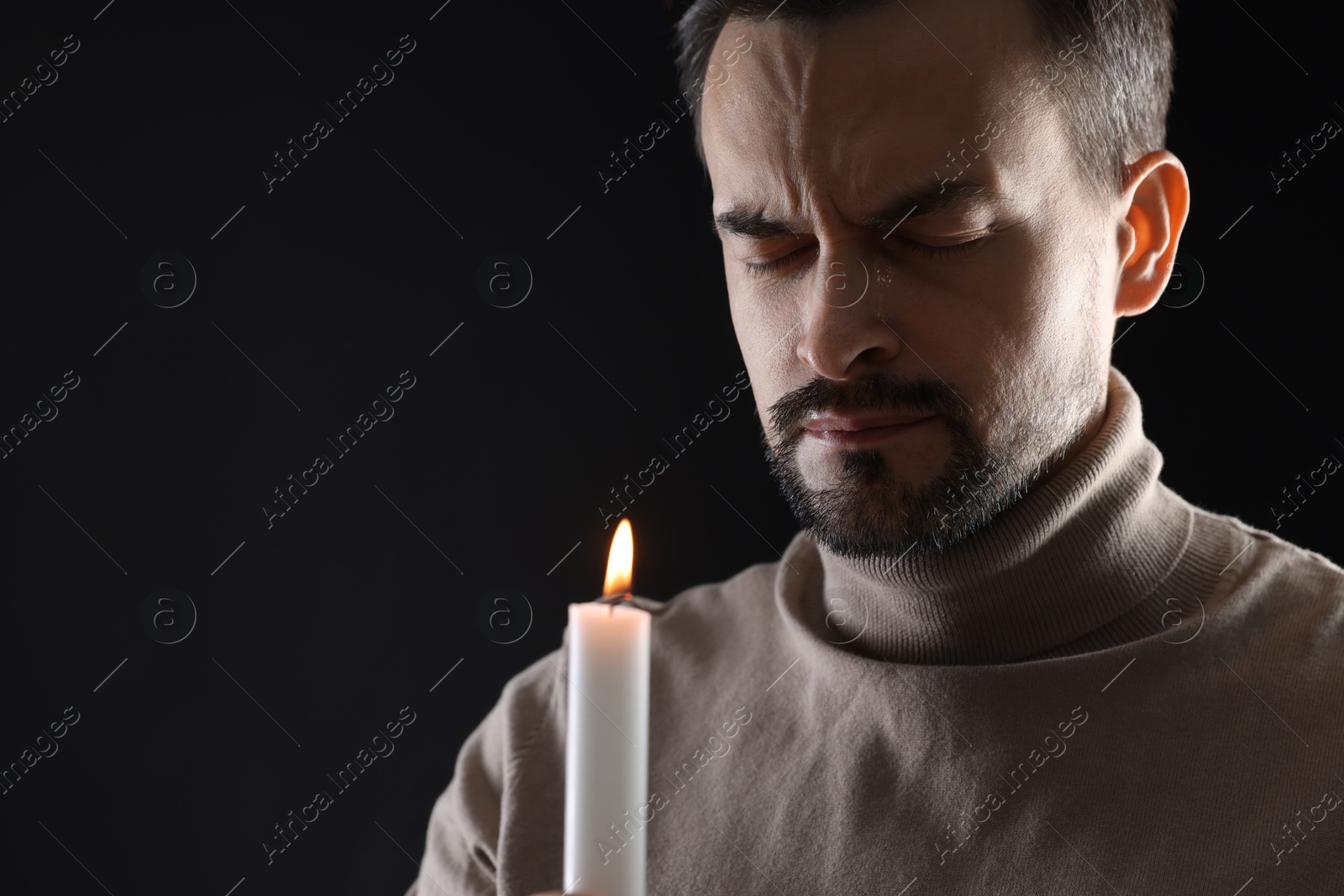 Photo of Sad man with burning candle crying on black background, space for text