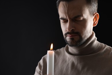 Sad man with burning candle crying on black background, space for text