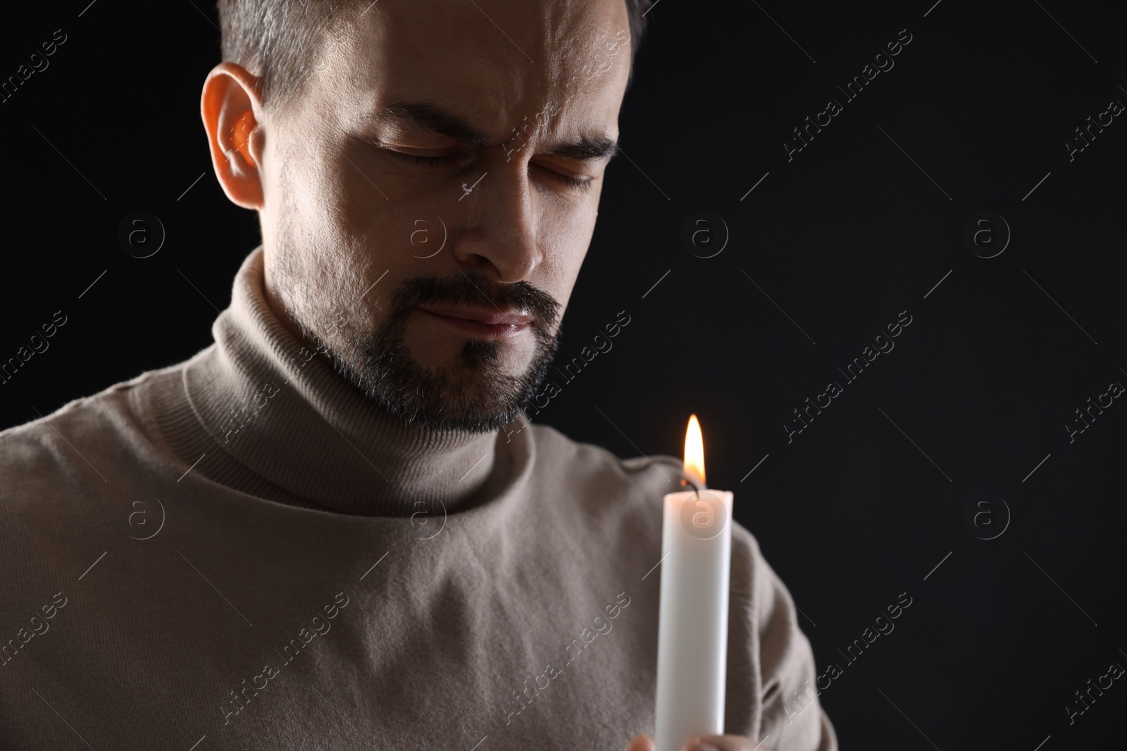 Photo of Sad man with burning candle crying on black background, space for text