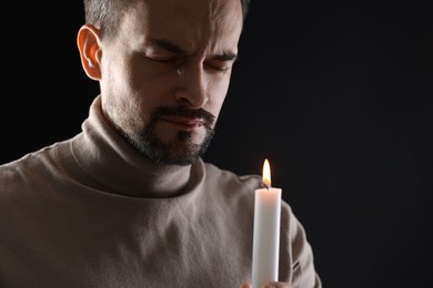 Photo of Sad man with burning candle crying on black background, space for text