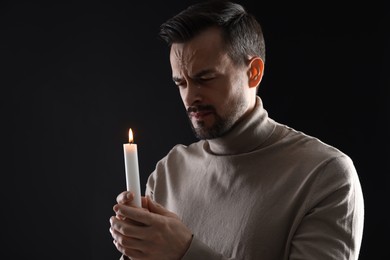 Photo of Sad man with burning candle crying on black background, space for text